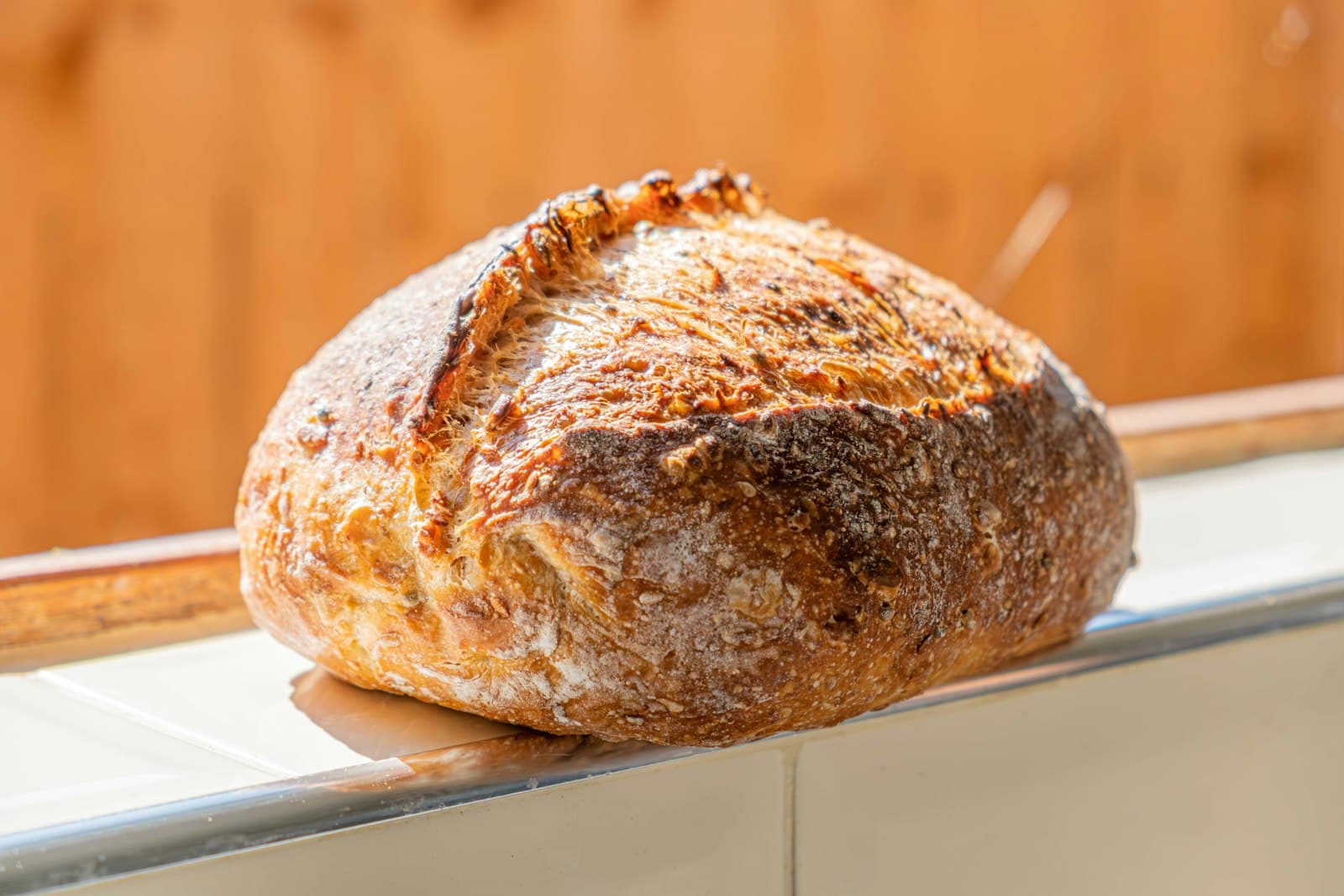 A sourdough loaf on a wooden board next to a small bunch of rosemary.