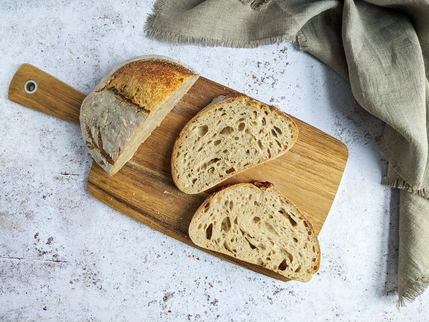 A round sourdough loaf with a deep score, sitting on a wooden board.