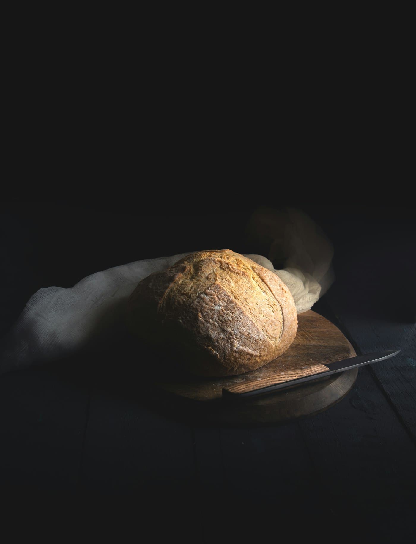 A dark-crusted artisan loaf beside a bread knife on a wooden board.