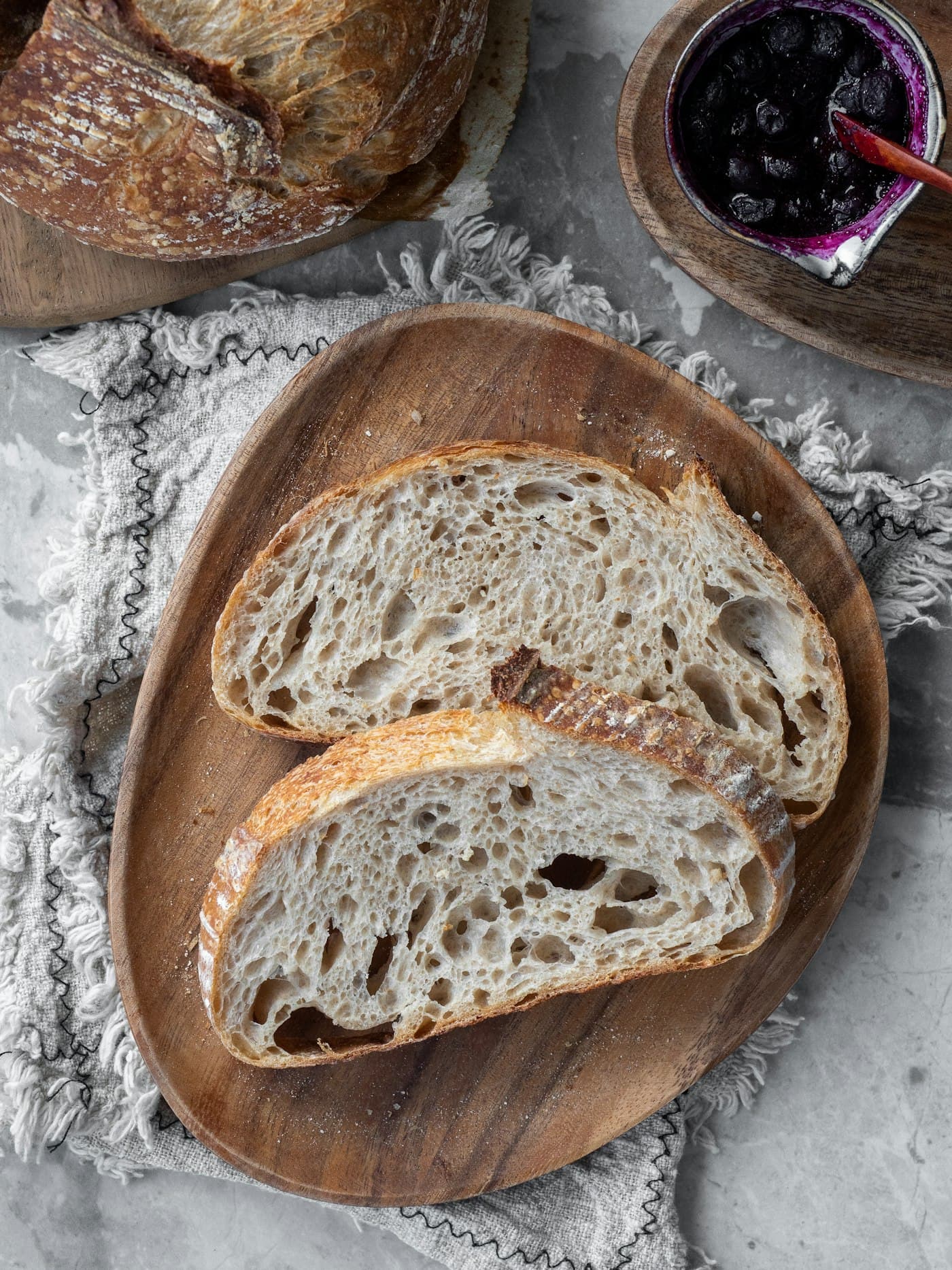 A flour-dusted round loaf in a wooden bowl, with a slice beside it.